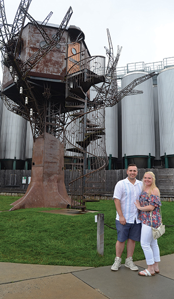 Dmitiry Shcherbenko and Brit Fossum stand in front of the Dogfish Tree on the Beer, Wine and Spirits Tour by Delmarva Discovery Tours